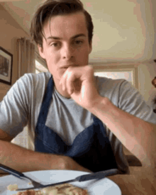 a man wearing an apron is sitting at a table with a plate of food