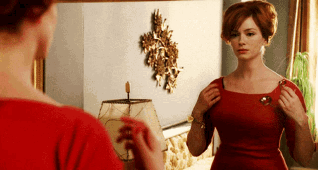 a woman in a red dress looks at herself in the mirror