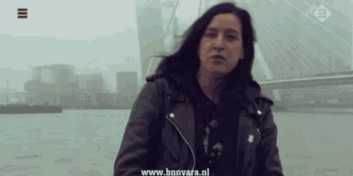 a woman in a leather jacket stands in front of a body of water