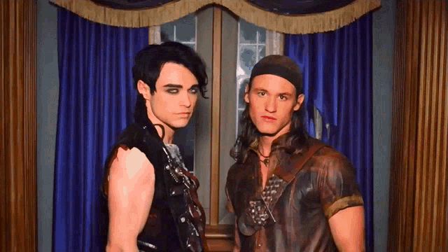 two men are standing next to each other in front of a blue curtain