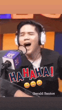 a man wearing headphones is laughing in front of a microphone and gerald santos is behind him