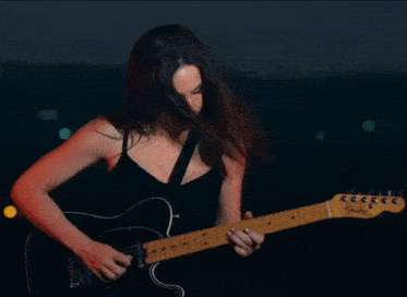 a woman is playing a fender guitar in a dark room