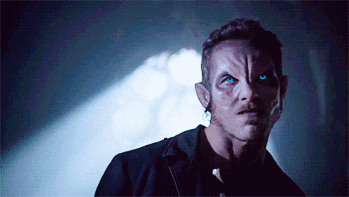 a man with blue eyes is standing in a dark room looking at the camera .