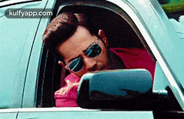 a man wearing sunglasses is sitting in a car and looking out the window .