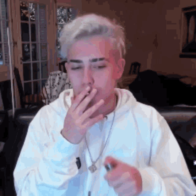 a man in a white hoodie is smoking a cigarette in a living room