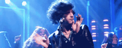 a man with curly hair singing into a microphone on stage