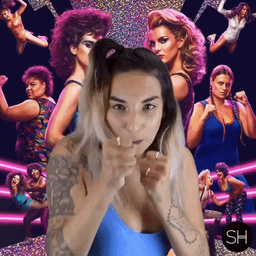 a woman in a blue leotard stands in front of a group of women with the letters sh on the bottom right