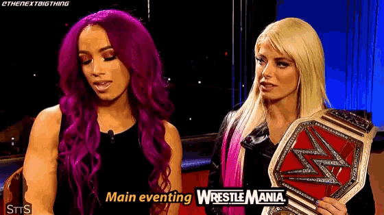 a couple of women standing next to each other holding a wrestling championship belt .