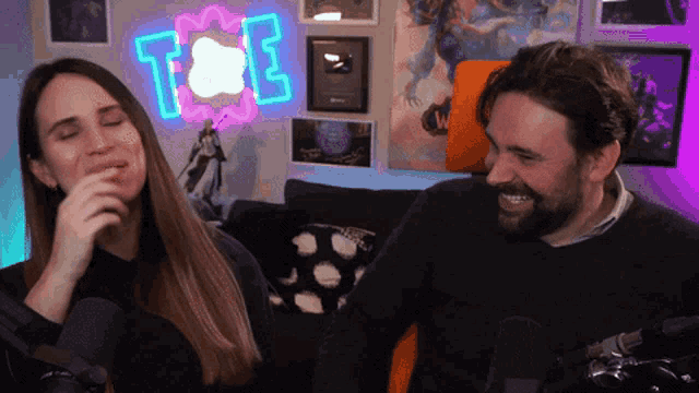 a man and a woman are sitting in front of a neon sign that says t & e