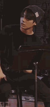 a man wearing a black shirt and a beanie is sitting in front of a microphone .