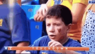a young boy sitting in a stadium watching a football game with the words touchdown on the screen
