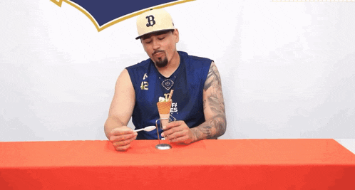 a man wearing a hat with the letter b on it holds a spoon