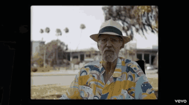 an older man wearing a hat and a colorful shirt is sitting in a chair ..
