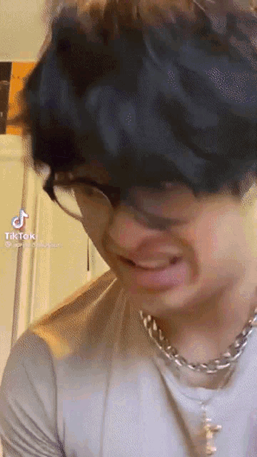 a young man wearing glasses and a necklace has a tiktok icon on his face