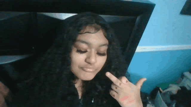 a girl with curly hair is giving the middle finger and has lipstick on her hand