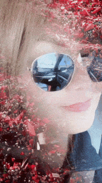 a woman wearing sunglasses is reflected in a car windshield