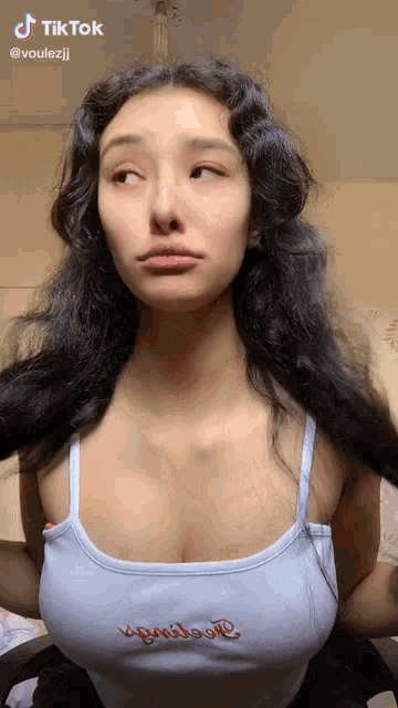 a woman with long dark hair is wearing a white tank top with the word love embroidered on it .