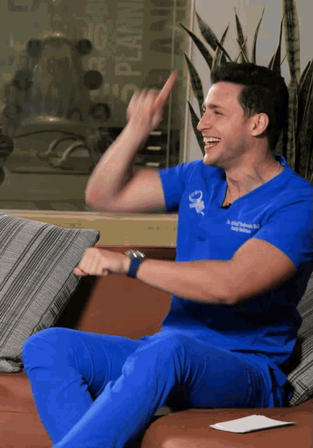 a man in a blue scrub top is sitting on a couch and pointing up