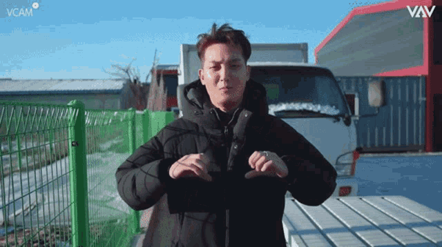 a man in a black jacket is standing in front of a white truck with the words vcam on the bottom