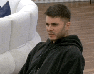 a man wearing a black hoodie is sitting on a couch .