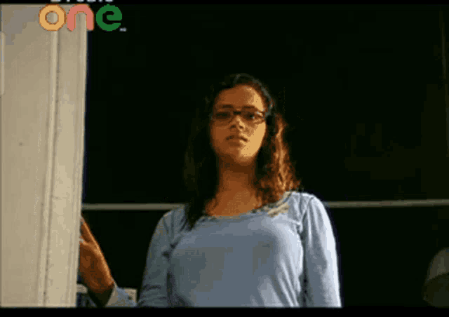 a woman wearing glasses and a blue shirt is standing in front of a door that says one