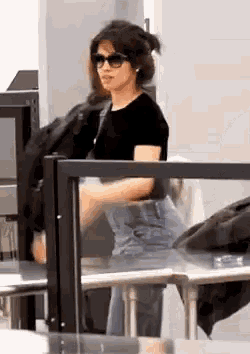 a woman wearing sunglasses and overalls is standing in front of a glass barrier