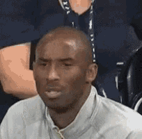 a man in a white shirt and tie is sitting in a stadium looking at something .