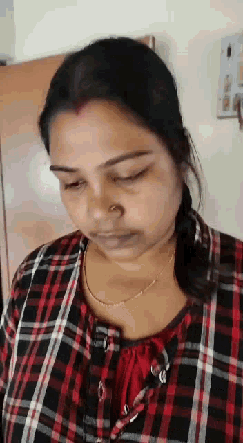 a woman wearing a plaid shirt and a nose ring looks down