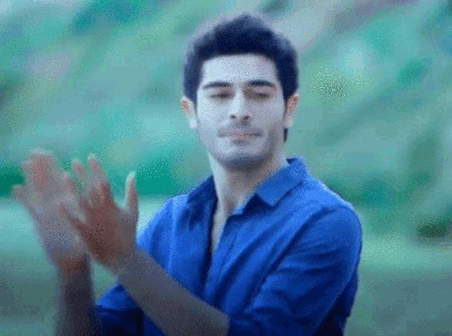 a man in a blue shirt applauds with his eyes closed