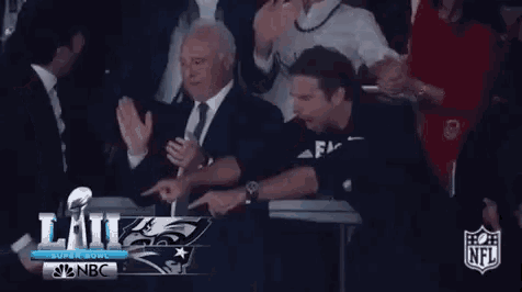 a man in a suit and tie is signing a football while sitting in a crowd .