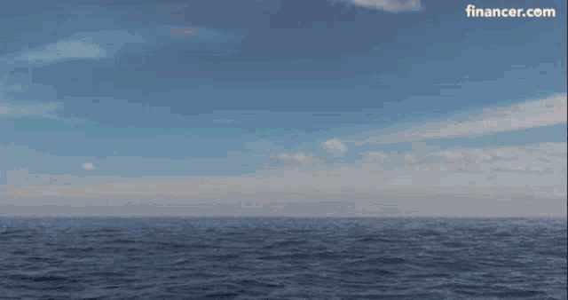 a box with a face on it is flying over the ocean with a financer.com logo in the corner