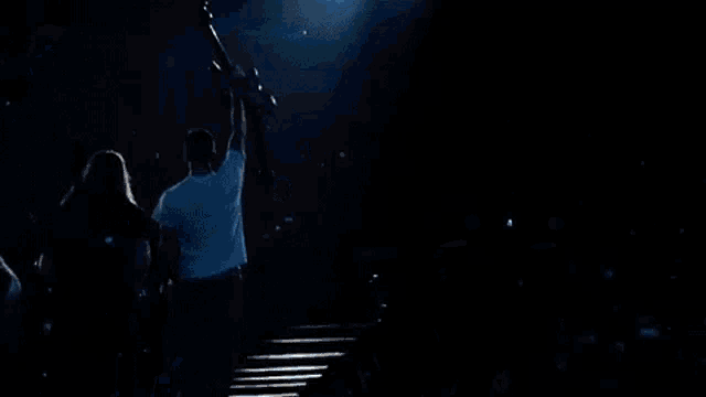 a man in a white shirt is holding a guitar in the air on a stage