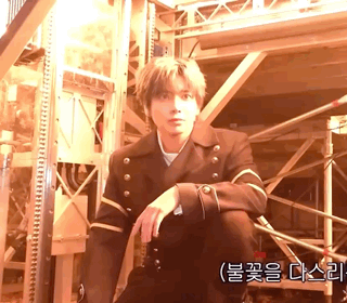 a man in a suit is kneeling down in front of a wooden structure with korean writing on the bottom