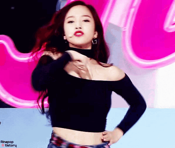a woman in a black off the shoulder top is dancing on a stage in front of a pink sign .