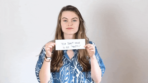 a woman holds up a sign that says " you don t have to be pretty "