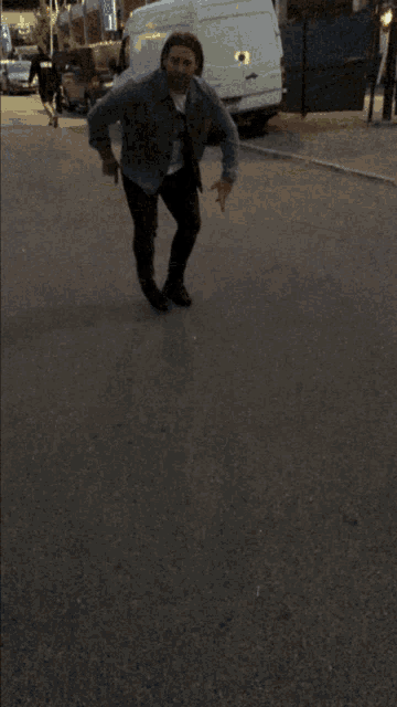 a man in a denim jacket and black pants is standing on a street