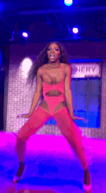 a woman in a pink bodysuit is dancing on a stage in front of a sign that says nerve
