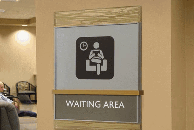 a sign for a waiting area with a person sitting in a chair