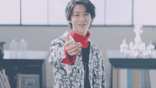 a young man wearing a leopard print jacket and a red turtleneck is giving a thumbs up