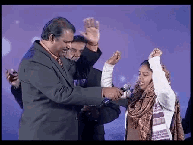 a man in a suit and tie holds a microphone in front of a woman with her hands in the air