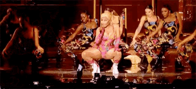 a group of women are dancing on a stage while a woman is sitting on the floor .