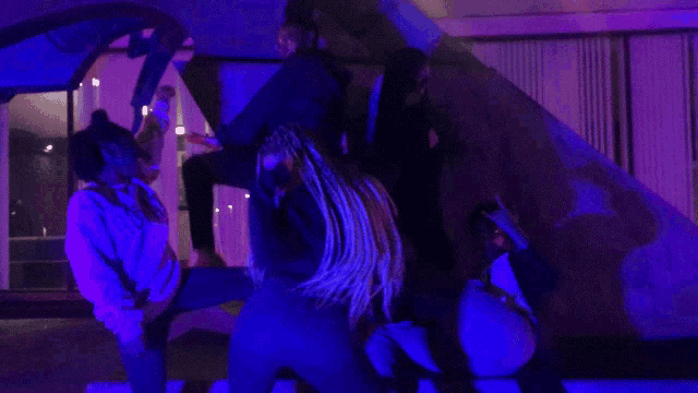 a group of people are dancing in front of a purple light