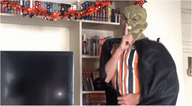 a man in a green mask is standing in front of a bookshelf with a game called overclocking on it
