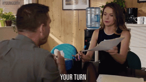 a man and woman are sitting at a table and the woman is holding a piece of paper that says your turn on it