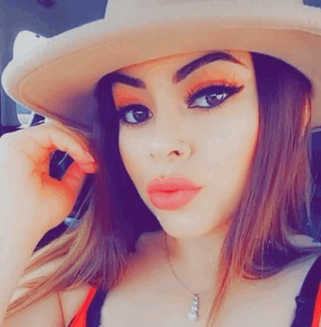 a woman wearing a cowboy hat and a necklace is taking a selfie in a car .