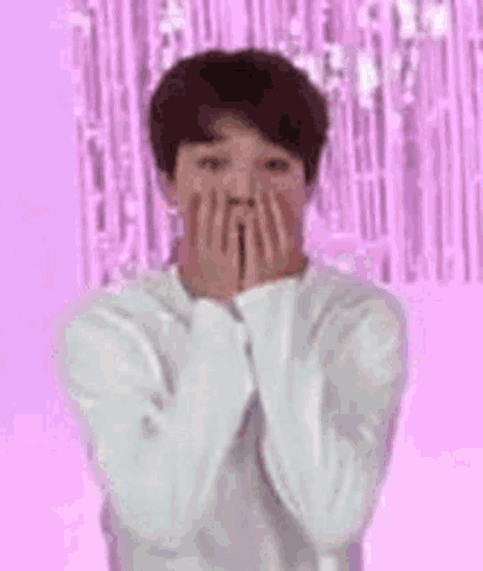 a boy is covering his face with his hands in front of a pink background with a cartoon character .