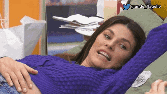 a woman in a purple sweater is laying on a green pillow with grande flagello written in the corner