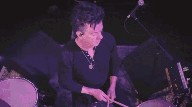a man in a black shirt is playing drums and singing into a microphone with a kb logo in the corner