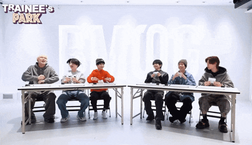 a group of young men are sitting at tables with trainee 's park in the background