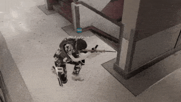 a soldier is kneeling down in a hallway holding a rifle .